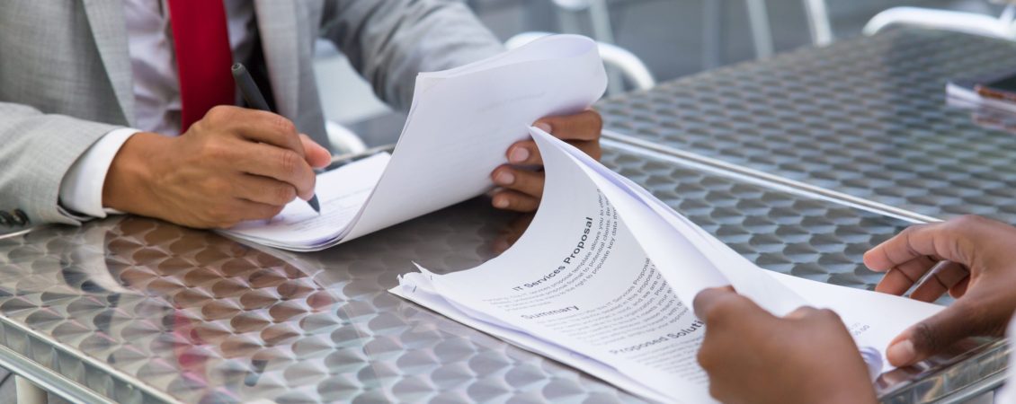 Business partners checking and signing documents in street cafe. Closeup of papers and writing business man hand. Deal or paperwork concept