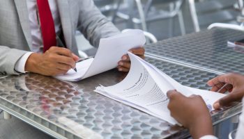 Business partners checking and signing documents in street cafe. Closeup of papers and writing business man hand. Deal or paperwork concept