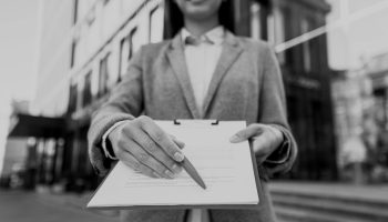 smiley-businesswoman-showing-you-where-to-sign-on-clipboard-darken